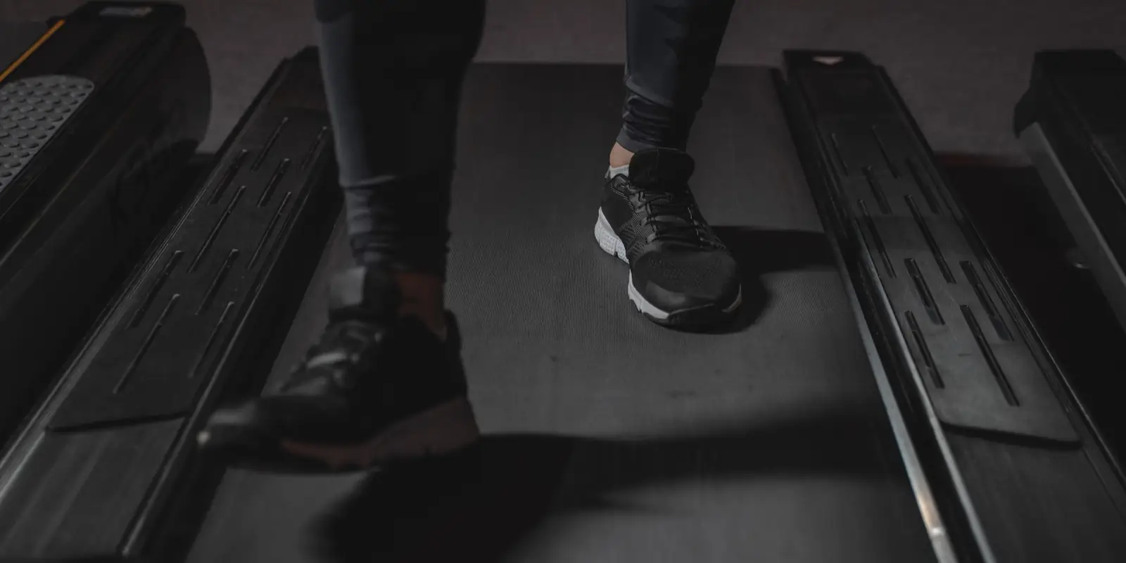 Close-up of feet in black trainers walking on a treadmill belt