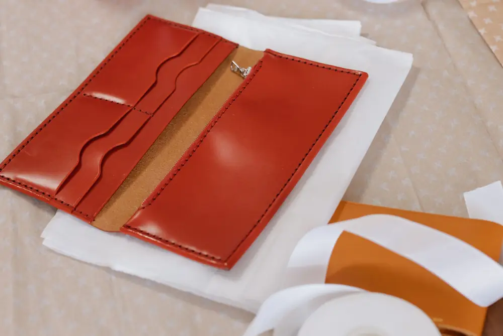An open red leather long wallet with card slots lying on white tissue paper next to gift ribbon