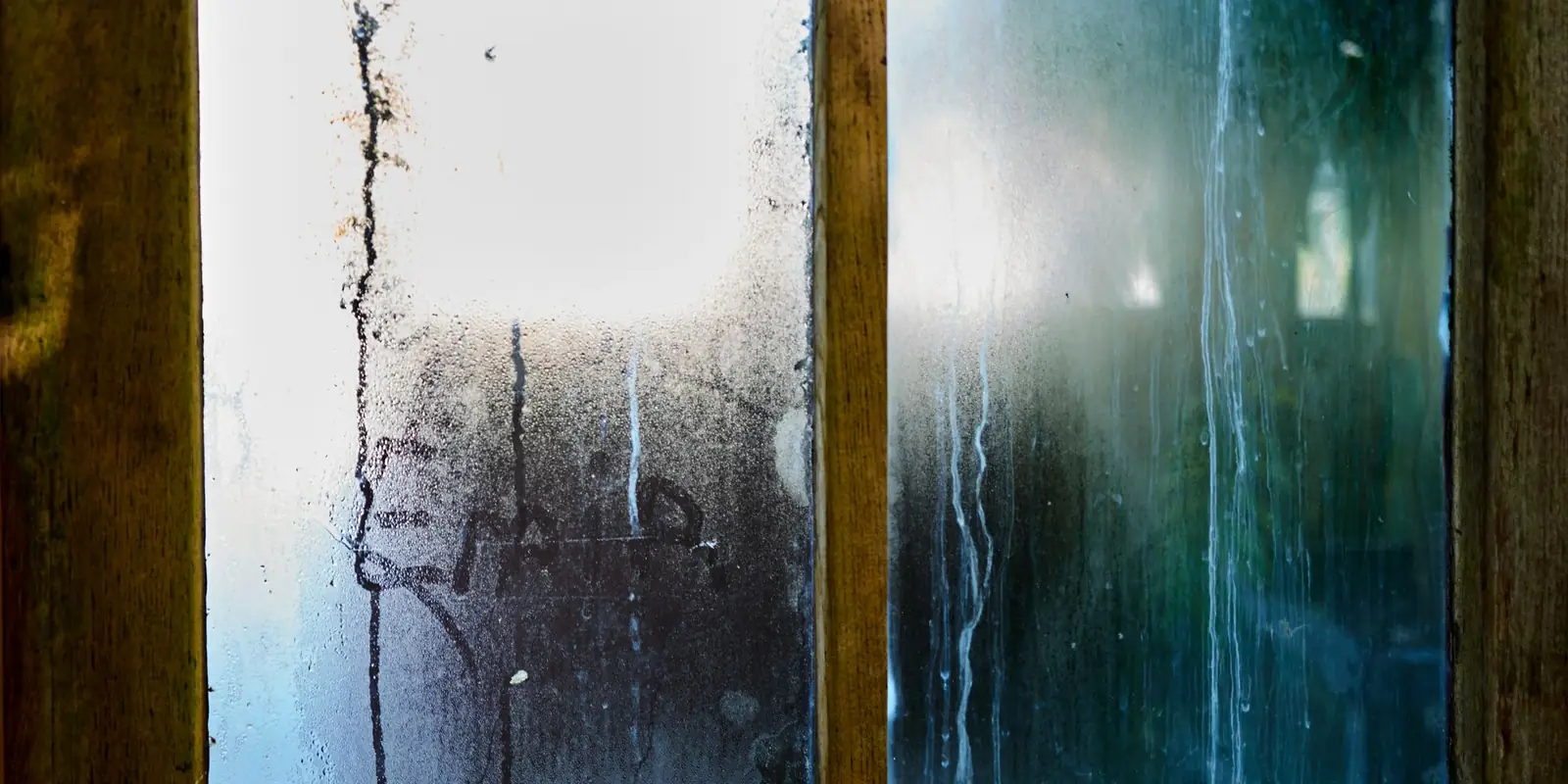 Condensation streaming down the inside of a wooden-framed window